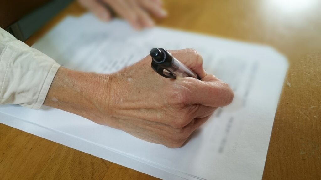 ボールペンで書類を記載している老人の手